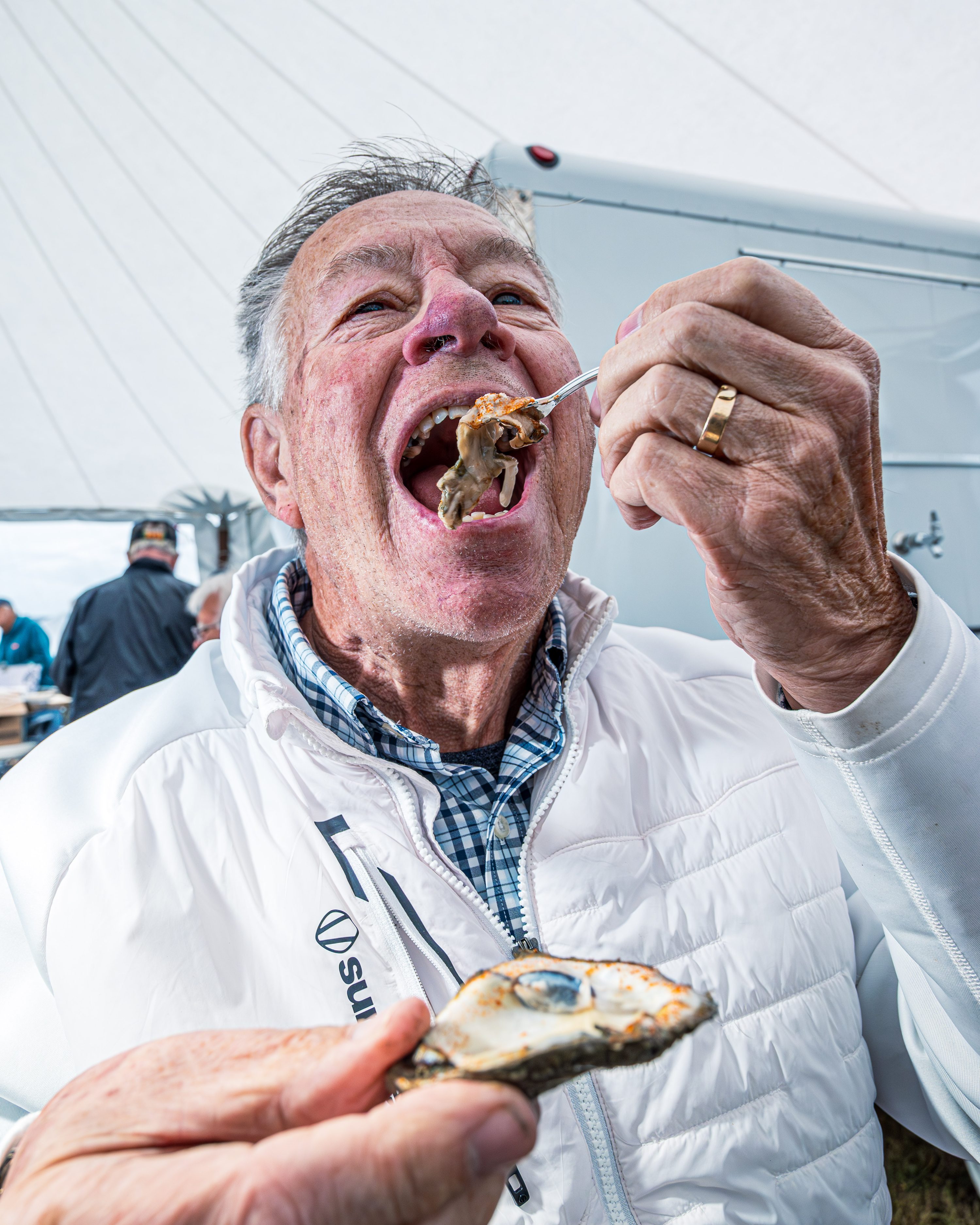 An older man eats oysters at a kitchen table in warm indoor light.
