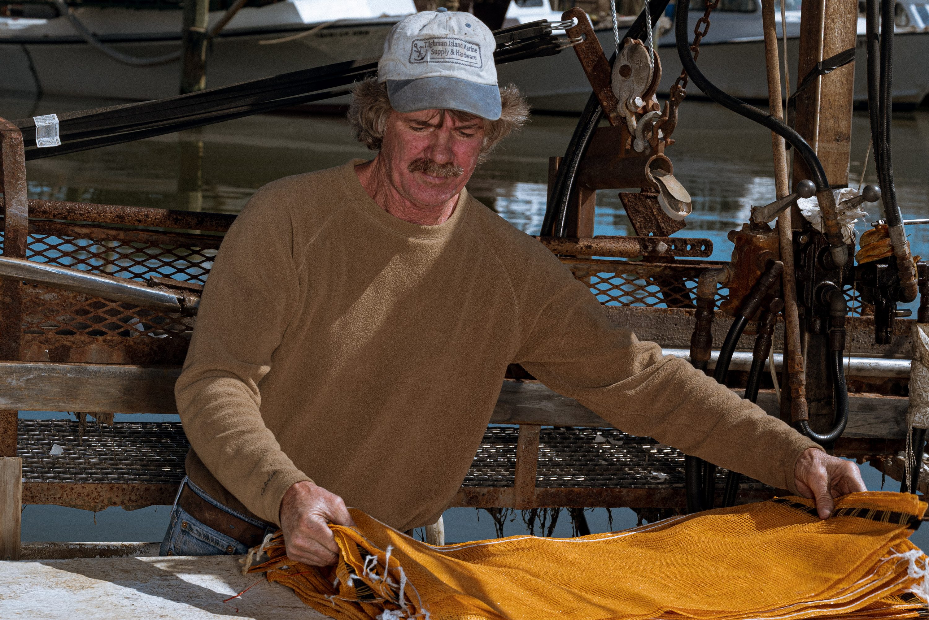 A waterman folds yellow oilskins on the deck of his boat.