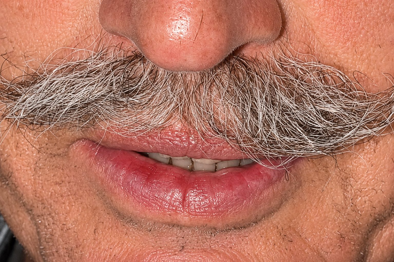 A tight close-up of a man’s grey mustache and soft smile.