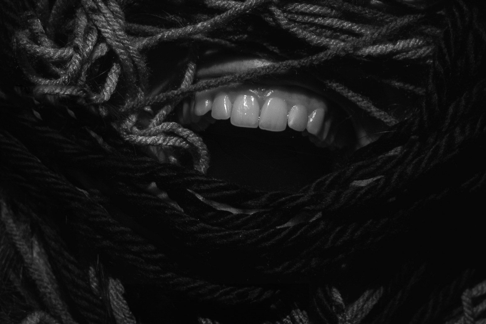 A mouth bites down on knotted rope, photographed in close-up.