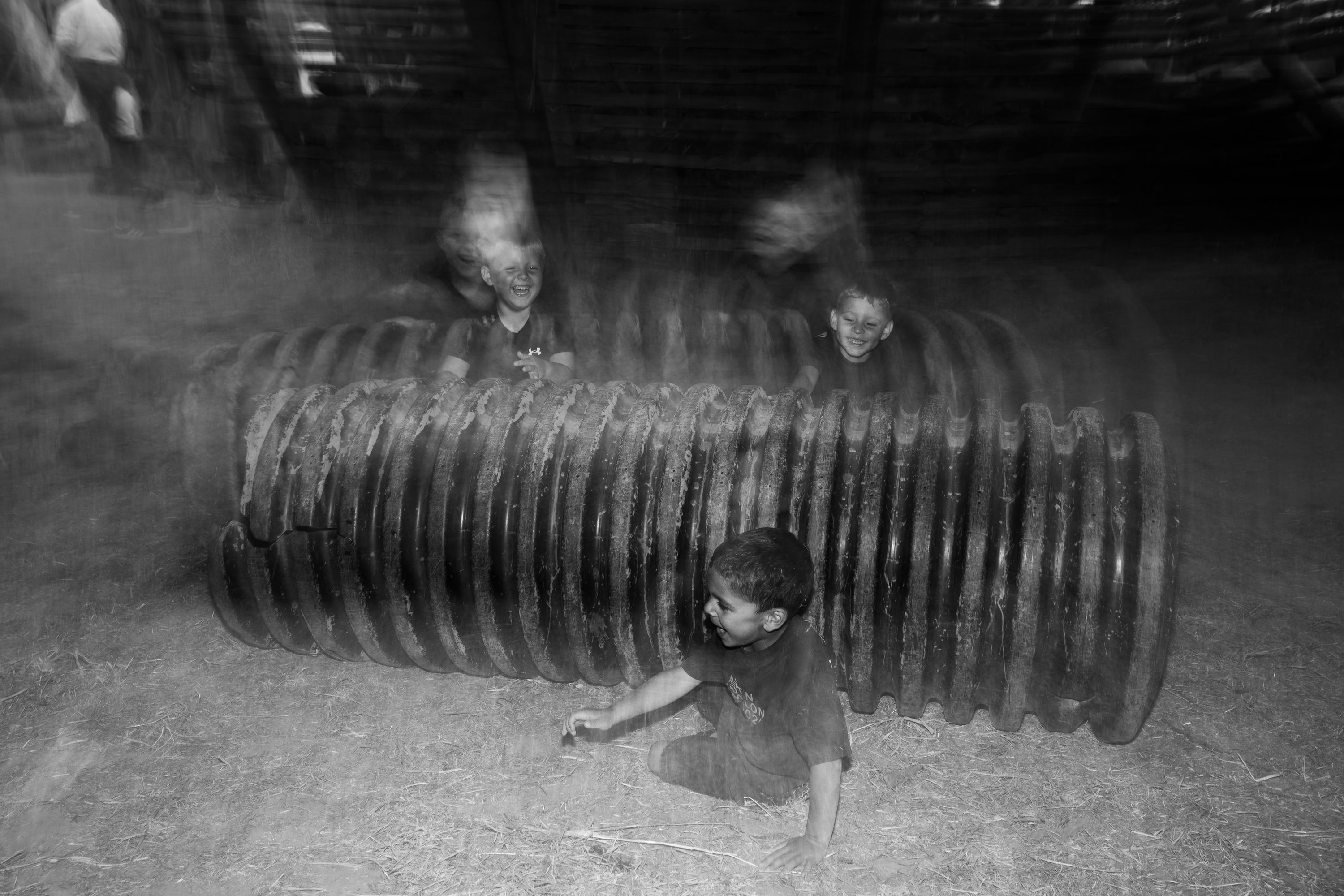 Children play inside a corrugated drainage pipe, in grainy black and white.