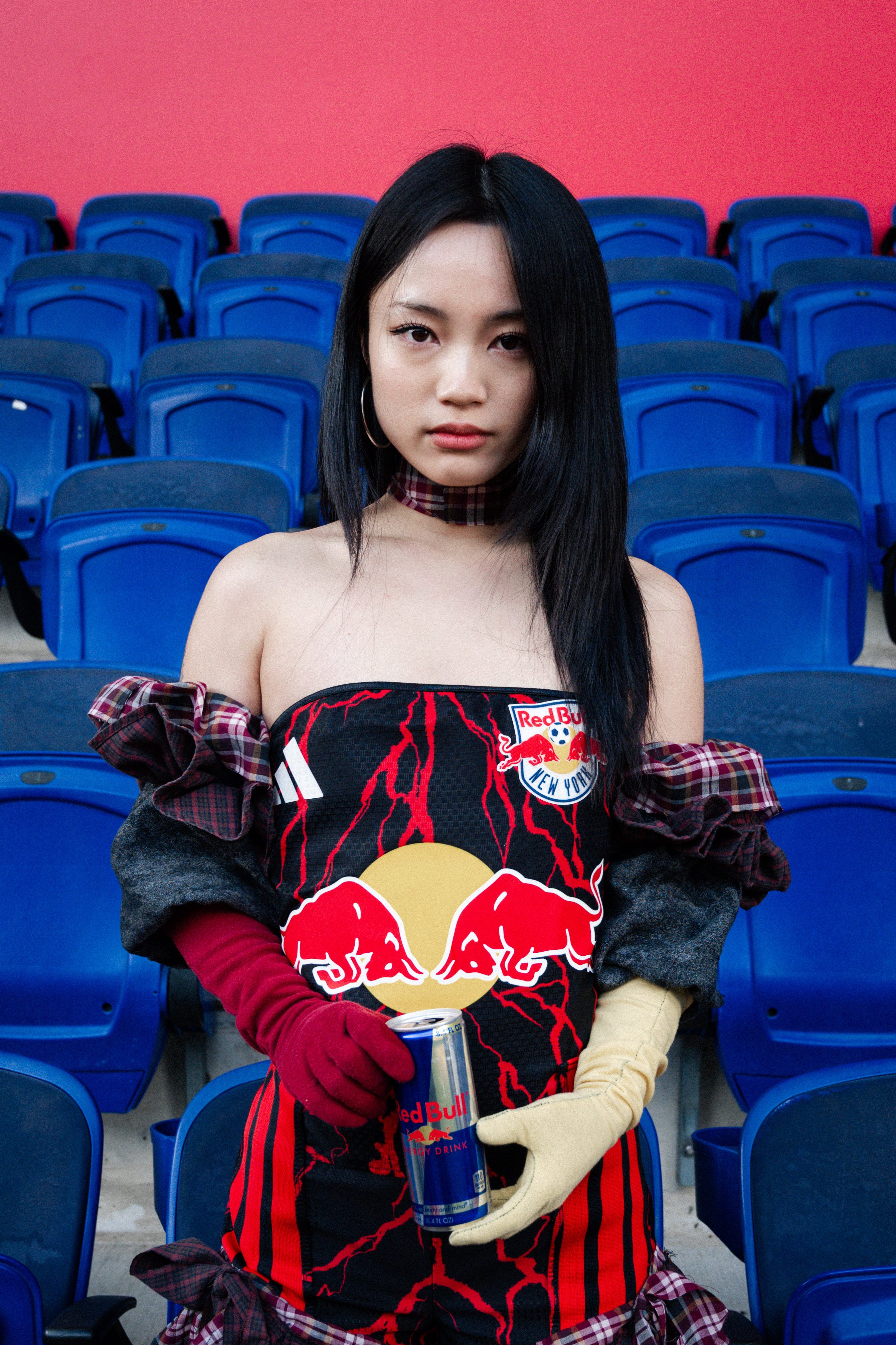 A woman in a Red Bull-branded dress stands among blue stadium seats.
