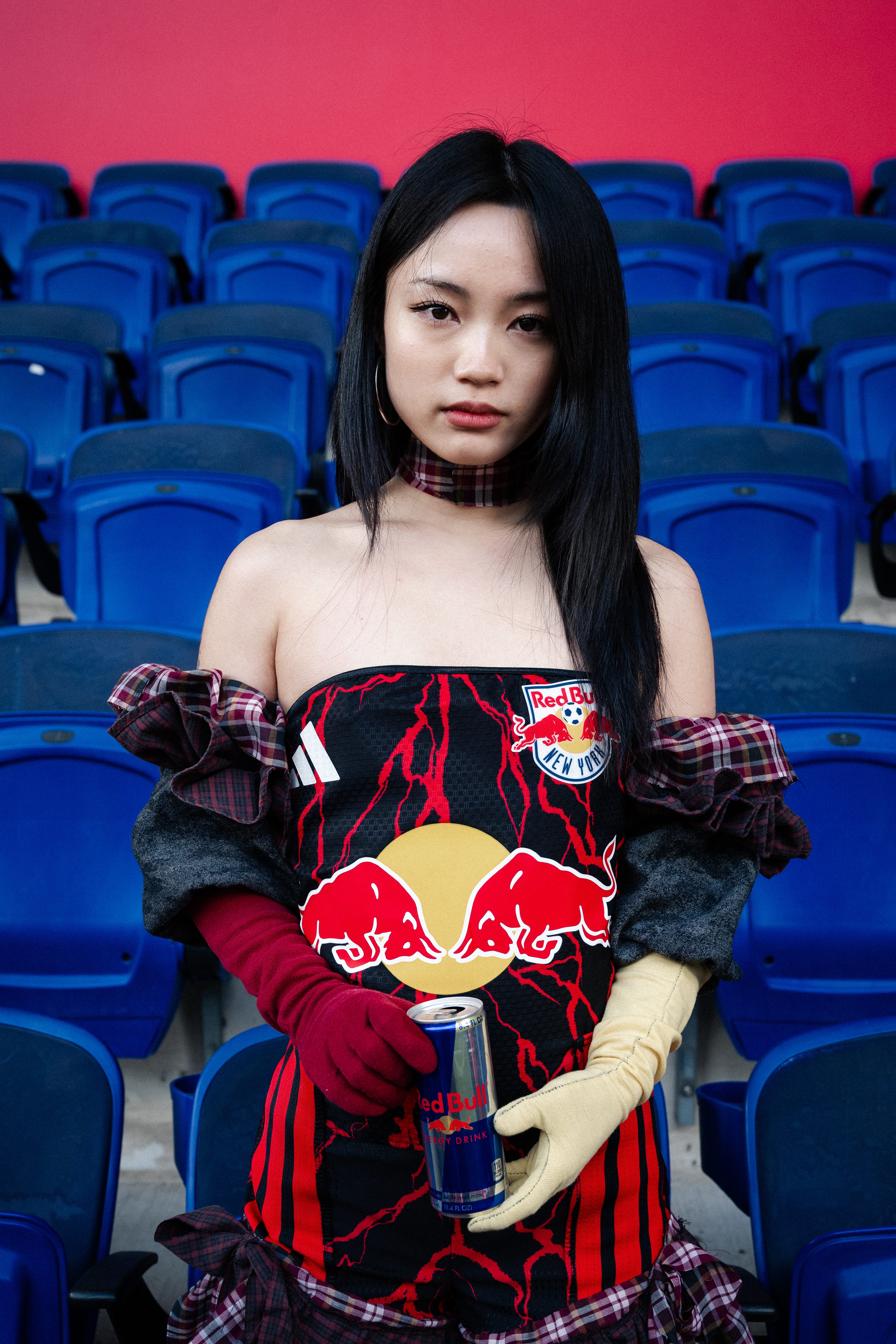 A woman in a Red Bull-branded dress stands among blue stadium seats.