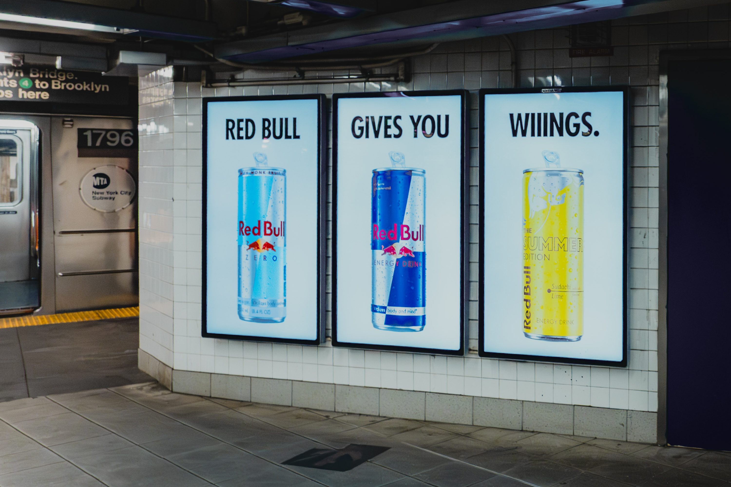 Red Bull cans glow in a lit cooler at a train station at night.